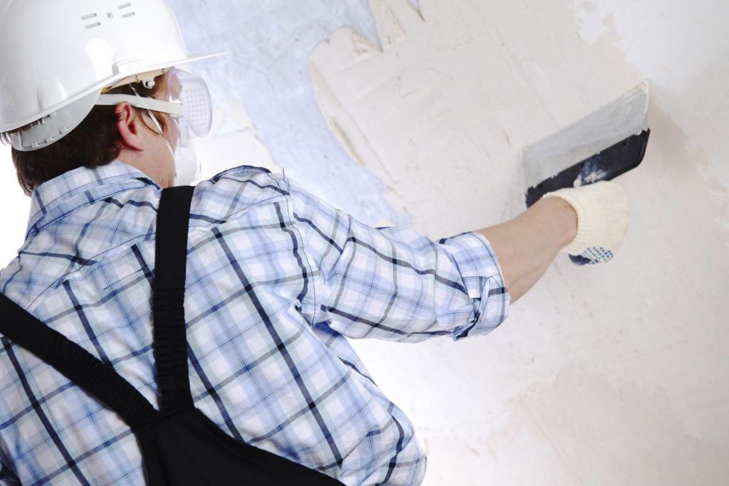 man wearing a safety helmet is applying plaster on the wall